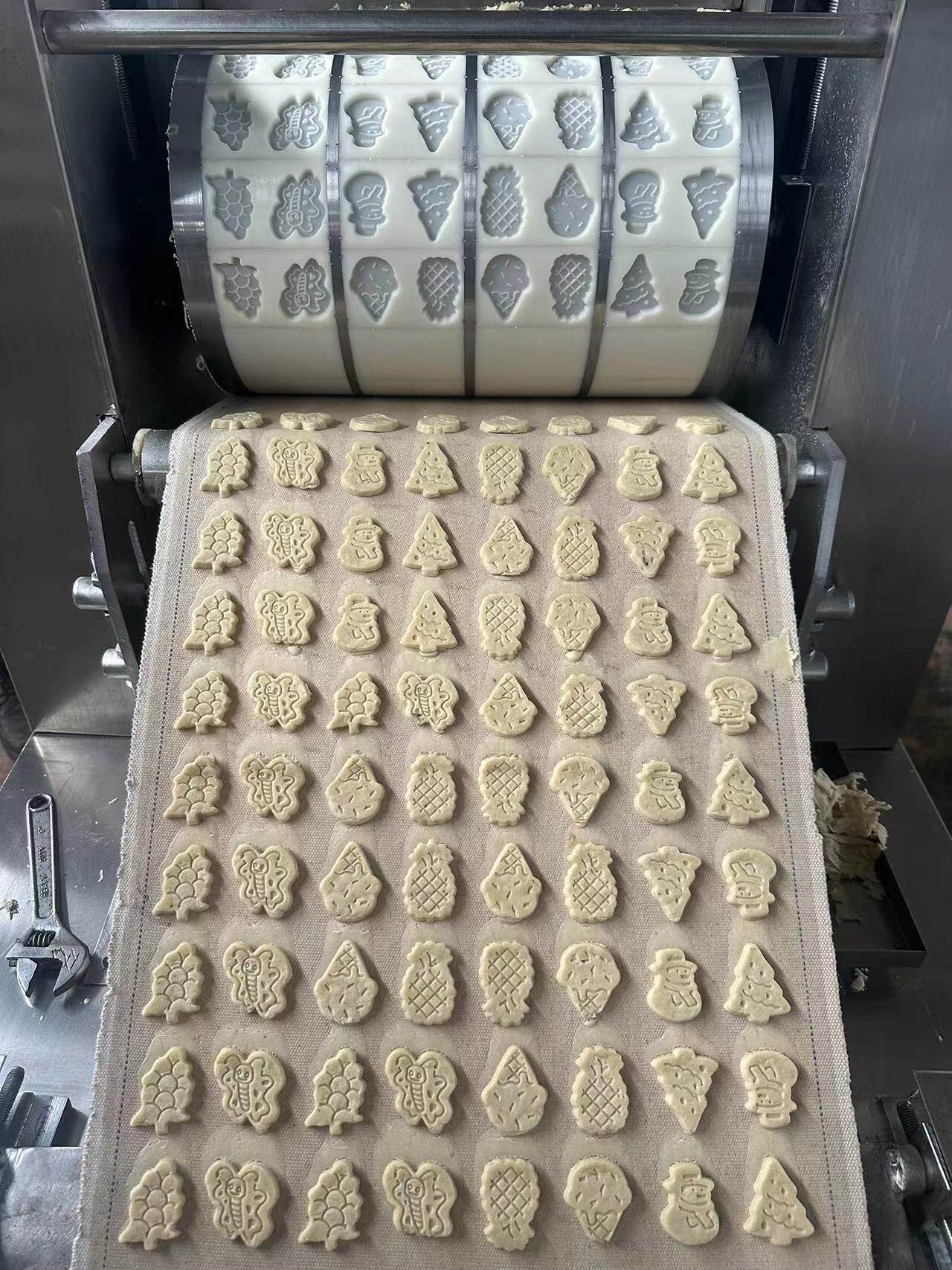 Shaped unbaked biscuit dough pieces below a patterned molding roller